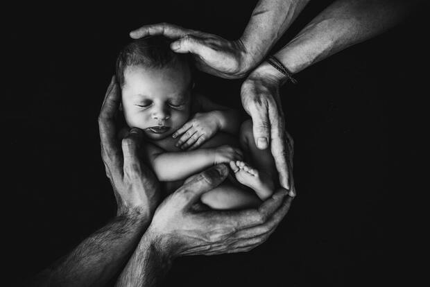 Two pairs of hands hold a newborn baby for support
