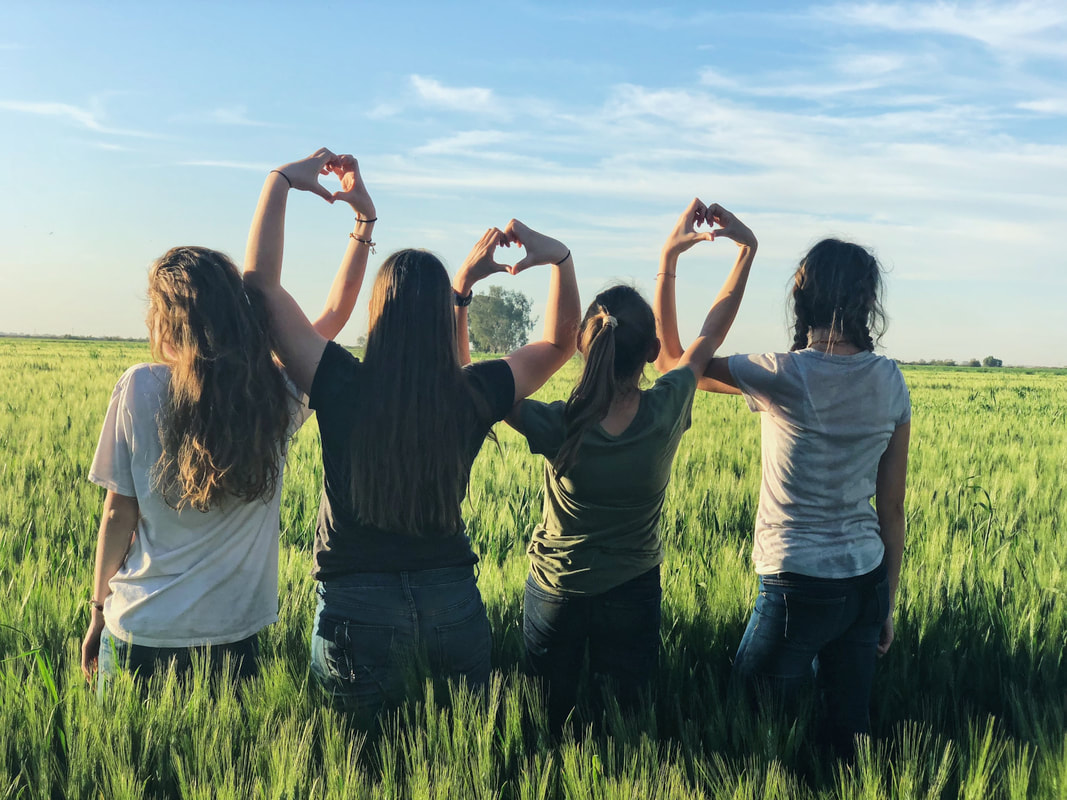 Women making hearts with their hands in a field